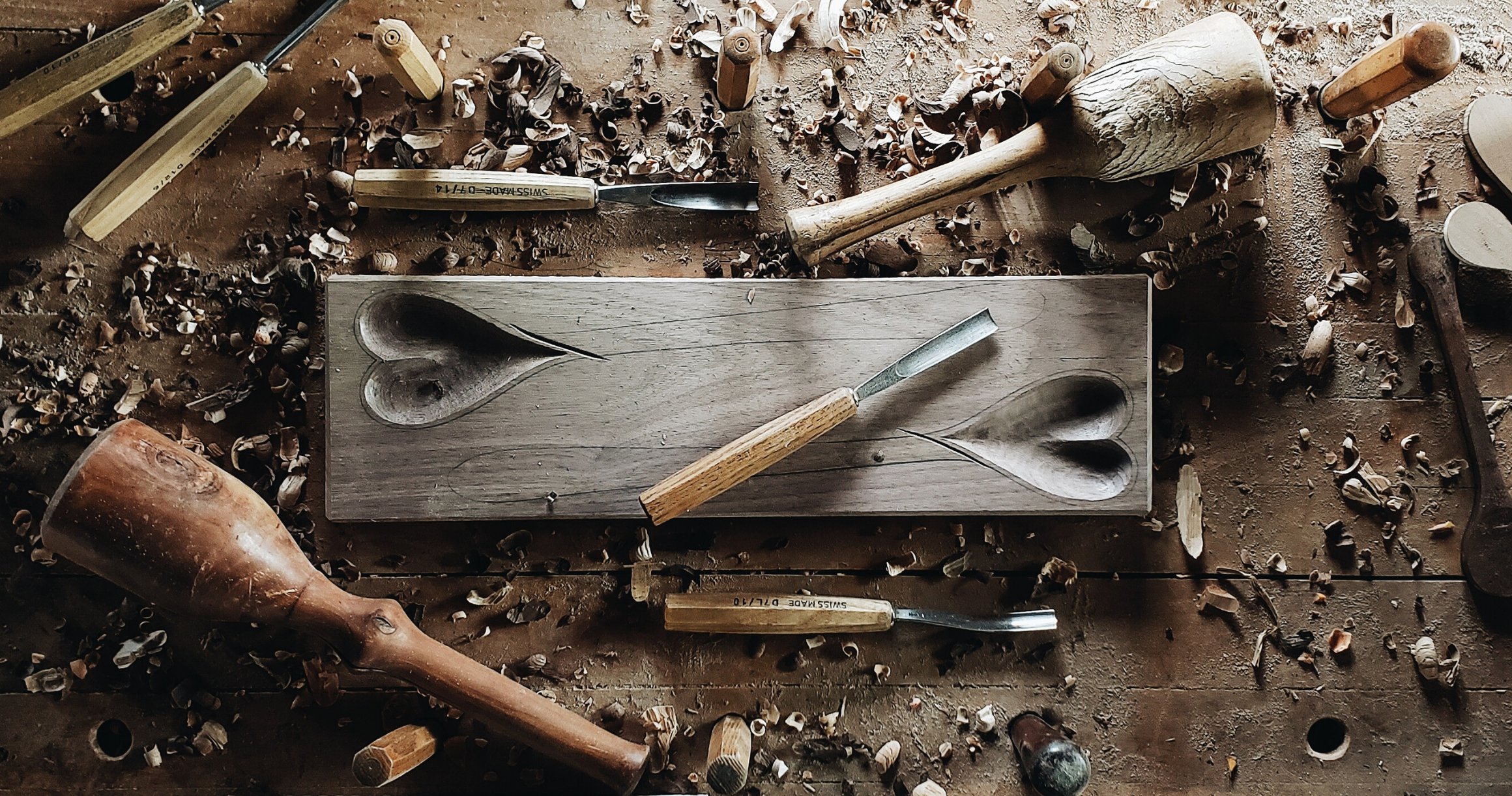 Photo of a workbench with carving tools and hearts carved from wood